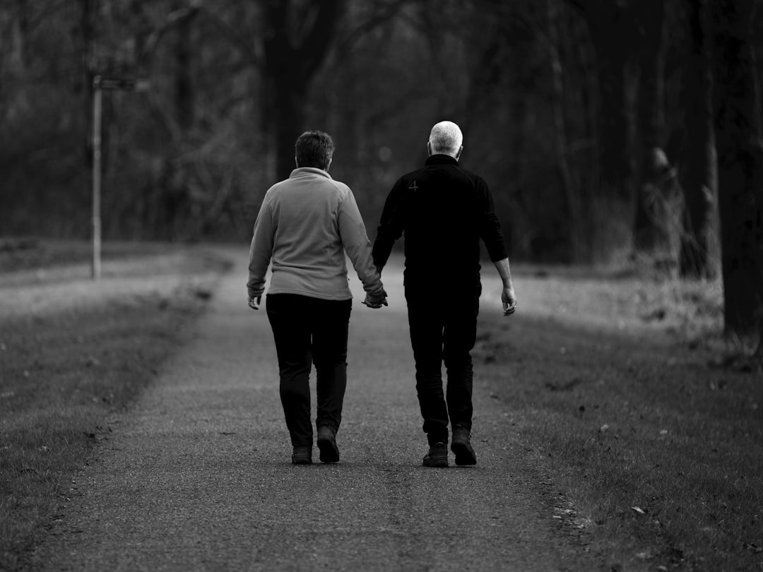 Two senior friends walking arm in arm through a park path